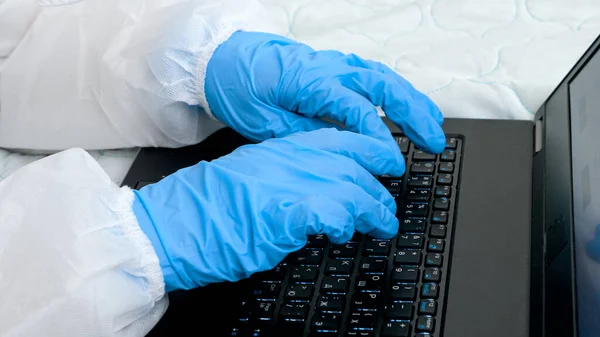 Närbild av händer som bär skyddande medicinska handskar skriva på laptop tangentbord. Arbete på distans bildar hem under nedstängning — Stockfoto