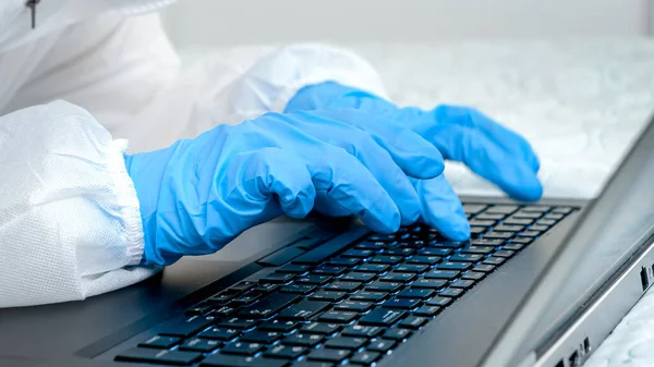 Närbild av läkare i medicinska skyddshandskar skriva på laptop tangentbord. Personer som skyddar mot covid-19 och coronavirus medan de arbetar på distans — Stockfoto