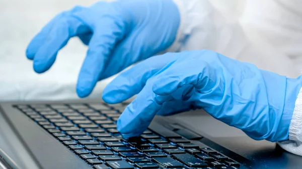Närbild av fingrar i medicinska handskar skriva på laptop tangentbord. Personer som arbetar hemifrån och skyddar från covid-19 — Stockfoto