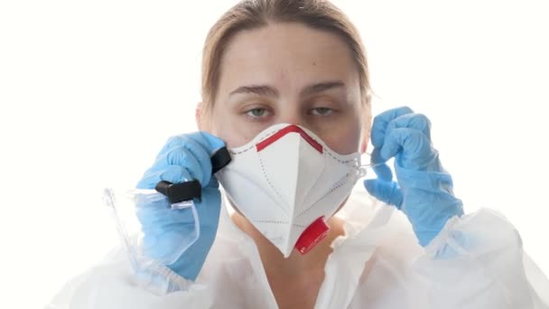 Portret młodej lekarki lub pracownika medycznego noszącego rękawiczki, maskę medyczną, garnitur i okulary ochronne na białym tle — Wideo stockowe