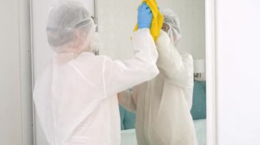 Koruyucu biyo-tehlike kıyafeti giyen biri kimyasal deterjanla evi temizliyor ve dezenfekte ediyor