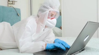 Koruyucu takım giyen serbest çalışan birinin portresi evde kalıp dizüstü bilgisayarla çalışıyor. GLobal covid salgını ve tecrit