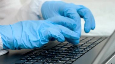 Laptop klavyesinde yazan tıbbi eldivenli parmaklar. Evden çalışan ve covid-19 'dan korunan insanlar.