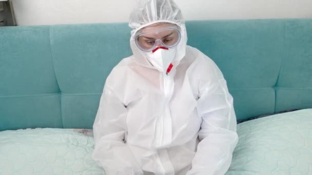 Mujer con máscara médica y traje de protección acostado en la cama y trabajando en el ordenador portátil. Trabajo remoto durante la pandemia mundial y covid-19 — Vídeo de stock