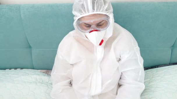 Koruyucu biyo-tehlike giysisi ve tıbbi solunum maskesi takan serbest çalışan bir işçi evde dizüstü bilgisayarla çalışıyor. Evde kalırken uzak çalışma — Stok video