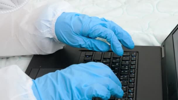 Primo piano delle mani che indossano guanti medici protettivi digitando sulla tastiera del computer portatile. Lavorare a distanza forma casa durante l'isolamento — Video Stock