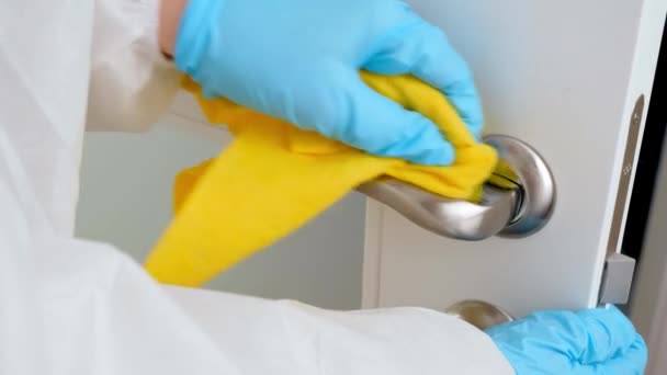 Detailní záběr ženy v ochranném lékařském obleku a rukavice čištění a mytí klik dveří doma.Lidé bojující proti covid-19 a coronavirus — Stock video