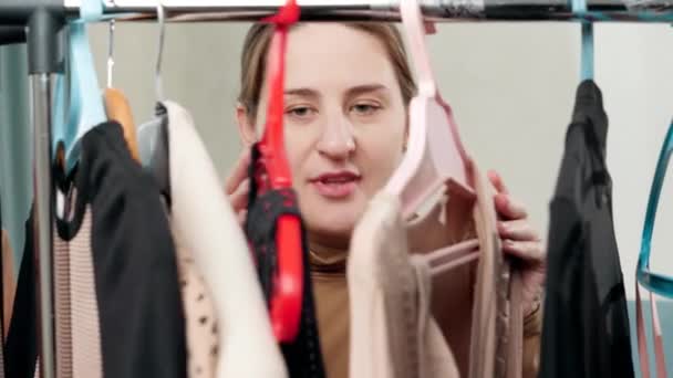 Портрет элегантной молодой женщины, стоящей в своем гардеробе и выбирающей платье для ношения — стоковое видео