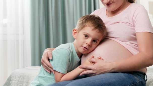 Porträt eines kleinen Jungen, der sein zukünftiges Baby im Bauch der schwangeren Mutter umarmt und zuhört — Stockvideo