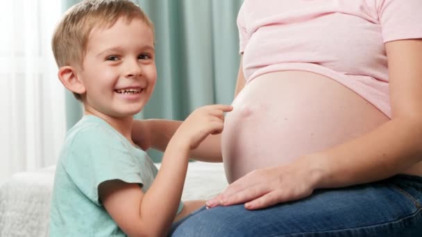 Glimlachend gelukkig jongetje kietelen en plezier hebben met grote zwangere buik van zijn moeder — Stockvideo