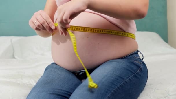 Terhes nő várja a babát mérőszalaggal, hogy ellenőrizze a méretét és a test paramétereit. A vemhes egészségügyi ellátás és az egészséges táplálkozás fogalma — Stock videók