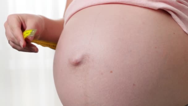 Крупный план женщины, ждущей ребенка, измеряющей талию и живот желтой измерительной лентой — стоковое видео