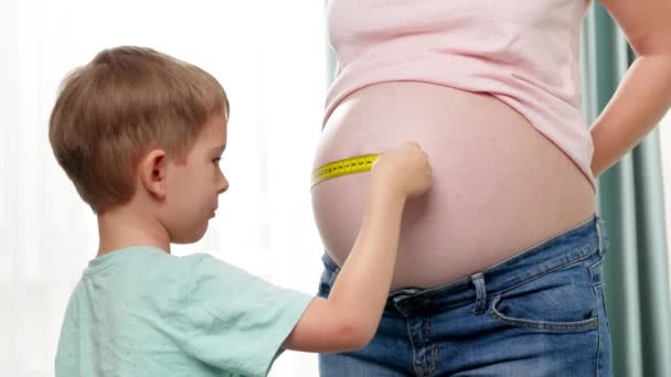 A kisgyerek segített a terhes anyjának megmérni a nagy hasát mérőszalaggal. Méret- és testparaméterek ellenőrzése terhesség alatt — Stock videók
