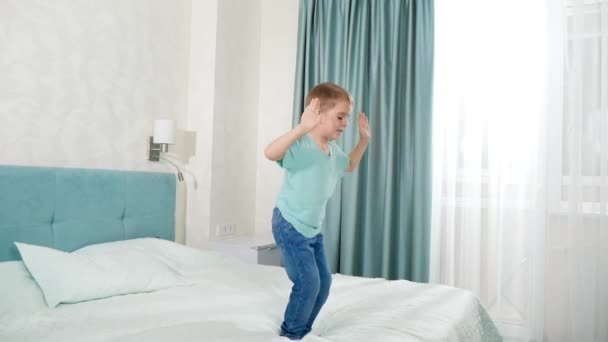 Långsam rörelse av glada barn pojke att ha kul och hoppa på sängen i sovrummet — Stockvideo