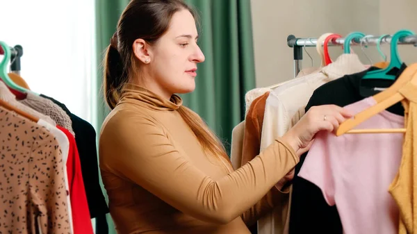 Portrait of woman searching for beautiful dress on hangers in shopping mall. — Stock Photo, Image