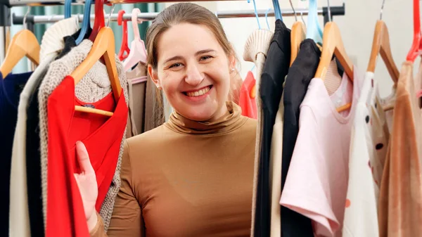 Красивая улыбающаяся женщина за длинной стойкой одежды на вешалках выбирает платье для ношения — стоковое фото