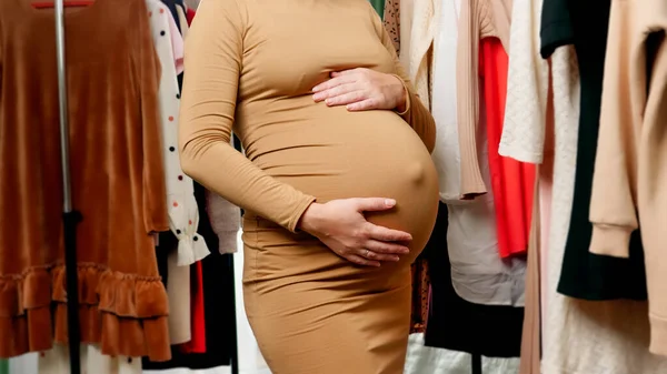 Închiderea femeii tinere însărcinate cu burta mare în rafturile mari ale mall-ului lungi de haine agățate pentru o femeie însărcinată — Fotografie, imagine de stoc