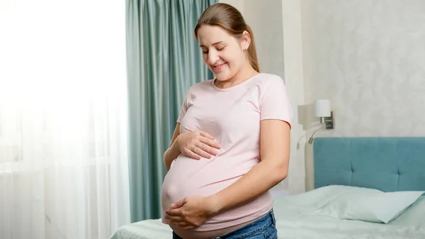 Retrato de mujer embarazada hermosa con gran vientre posando en la ventana en el dormitorio y mirando en la cámara —  Fotos de Stock