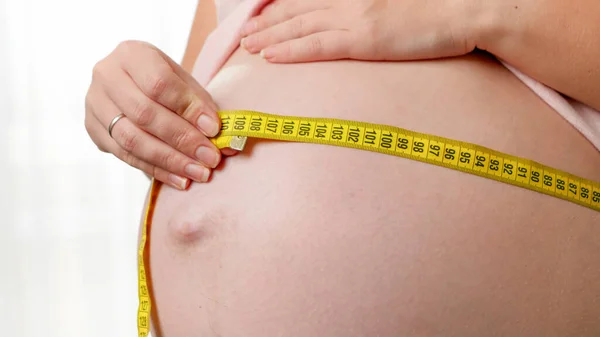Крупный план женщины, ждущей ребенка, измеряющей талию и живот желтой измерительной лентой — стоковое фото
