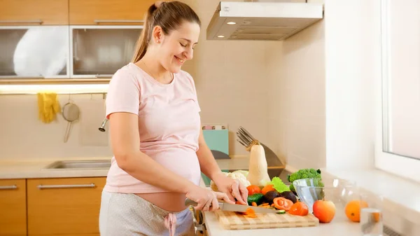 Усміхнена молода жінка чекає на дитину, готує на кухні і виконує домашні завдання. Концепція здорового способу життя та харчування під час вагітності — стокове фото