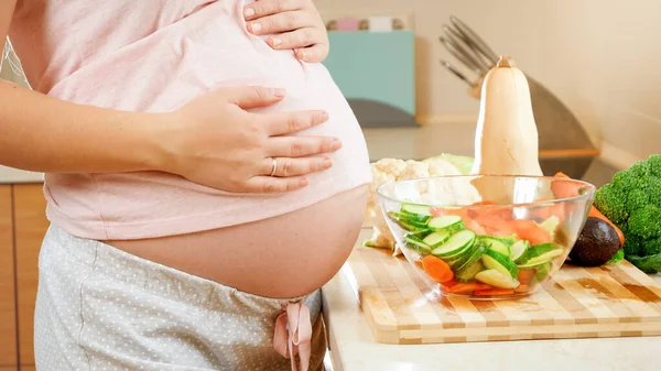 Zbliżenie ciężarnej kobiety z dużym brzuchem stojącej na kuchni i dotykającej dużego brzucha. Pojęcie zdrowego trybu życia i odżywiania w czasie ciąży — Zdjęcie stockowe