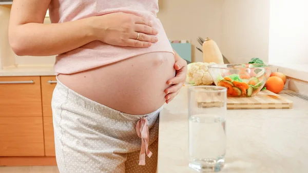 Güzel hamile bir kadının bir bardak suyu alıp mutfakta içtiği fotoğraf. Hamilelik boyunca sağlıklı yaşam biçimi, beslenme ve susuzluk kavramı — Stok fotoğraf