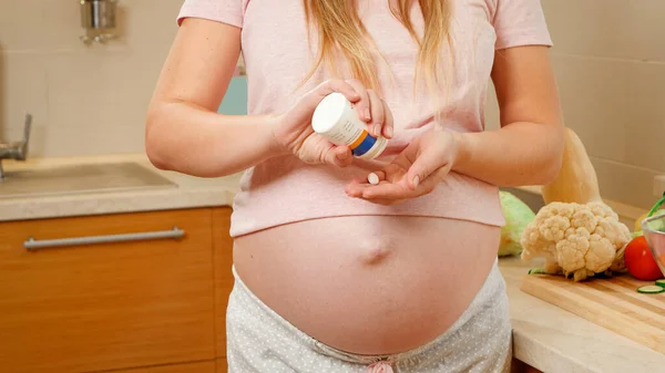 CLoseup de la mujer embarazada verter píldoras vitamínicas en la mano desde el envase de plástico botella. Concepto de estilo de vida saludable, nutrición e hidratación durante el embarazo — Foto de Stock