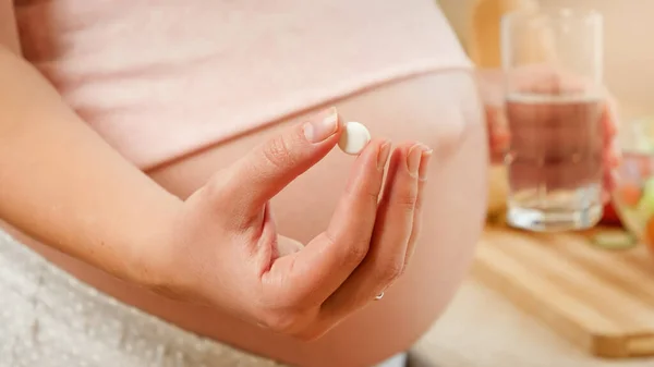 CLoseup van zwangere vrouw met glss water en medische pil of vitaminen in de hand. Concept van gezonde levensstijl, voeding en hydratatie tijdens de zwangerschap — Stockfoto