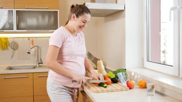 Felice donna incinta sorridente tagliare le verdure e cucinare in cucina a casa. Concetto di stile di vita sano e nutrizione durante la gravidanza — Video Stock