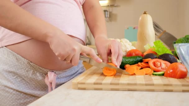 Крупный план беременной женщины с большим животом режет овощи и приготовления салата на кухне. — стоковое видео