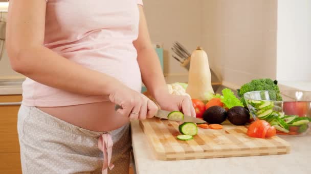 Улыбаясь беременной вумен делает салат и ест свежий огурец на кухне в доме. Концепция здорового образа жизни и питания во время беременности — стоковое видео