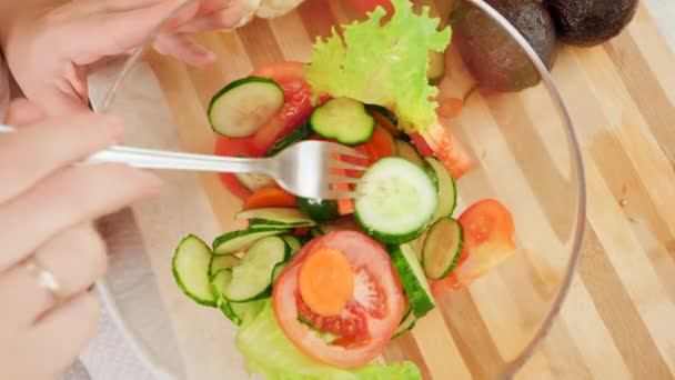 Вид сверху на женщину, смешивающую свежие овощи и делающую вкусный салат в большой стеклянной миске на кухне — стоковое видео