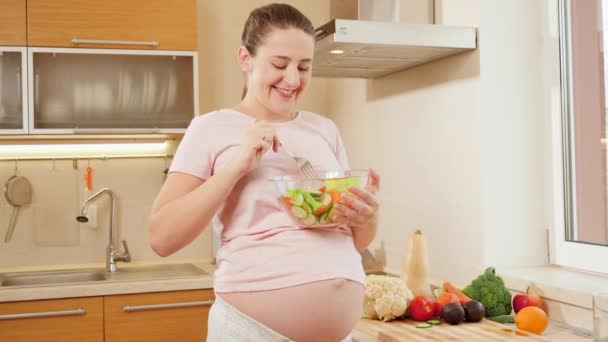 Ritratto di donna incinta sorridente che tiene una grande ciotola di vetro e mangia insalata di verdure in cucina — Video Stock