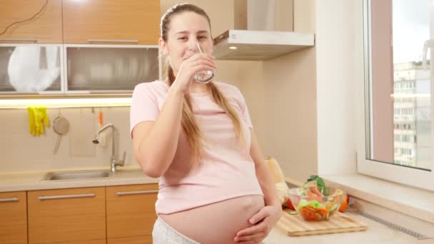 Ευτυχισμένη έγκυος γυναίκα πίνει νερό στην κουζίνα το πρωί και χαμογελά στην κάμερα — Αρχείο Βίντεο