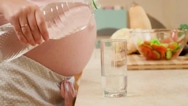 Primo piano di donna incinta versando l'acqua in vetro da bottiglia di plastica su cucina di mattina. Concetto di stile di vita sano, nutrizione e idratazione durante la gravidanza — Video Stock