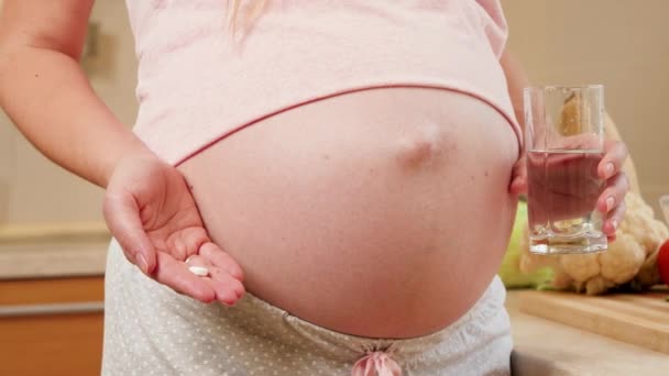 Closeup της εγκύου γυναίκα περιμένει το μωρό κρατώντας ιατρικό χάπι ή βιταμίνες και ένα ποτήρι καθαρό νερό. Έννοια υγιεινού τρόπου ζωής, διατροφής και ενυδάτωσης κατά την εγκυμοσύνη — Αρχείο Βίντεο