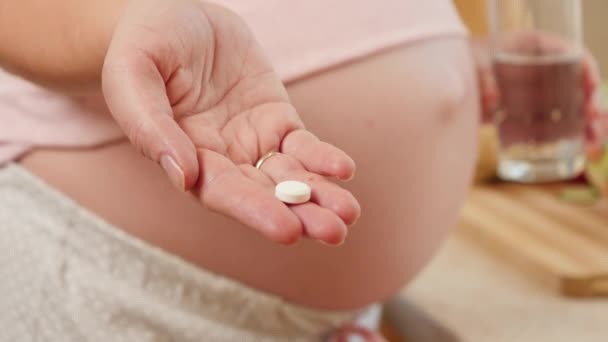 Κοντινό πλάνο της νεαρής γυναίκας που περιμένει μωρό κρατώντας ιατρικό χάπι ή βιταμίνη στο χέρι. Έννοια υγιεινού τρόπου ζωής, διατροφής και ενυδάτωσης κατά την εγκυμοσύνη — Αρχείο Βίντεο