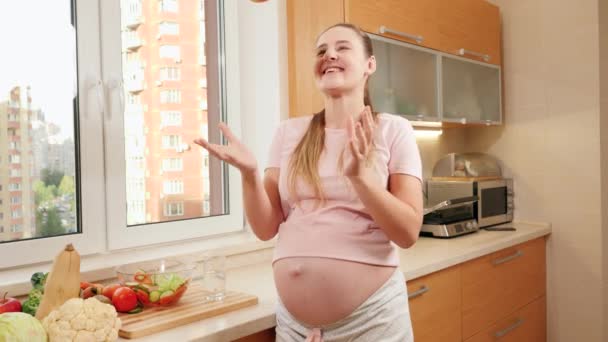 Felice donna incinta sorridente gettando e catturando mela matura rossa in cucina mentre fa colazione. Concetto di stile di vita sano, nutrizione e idratazione durante la gravidanza — Video Stock