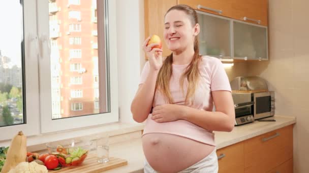 Portrait of happy smiling pregnant woman with big belly holding fresh ripe apple and looking in camera. Concept of healthy lifestyle, nutrition and hydration during pregnancy — Stock Video