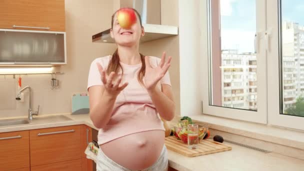 Glad leende gravid kvinna kasta färska mogna äpple medan du äter frukost på köket. Begreppet hälsosam livsstil, kost och hydrering under graviditeten — Stockvideo