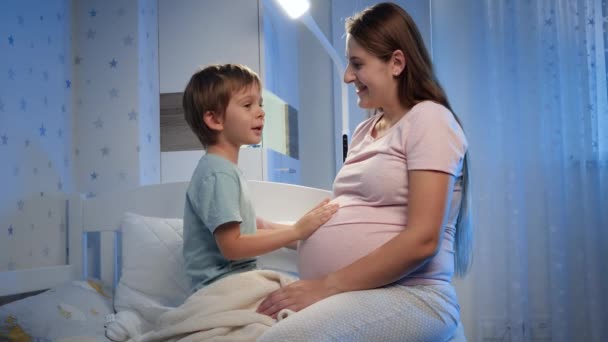 Malý batole chlapec hladí a hladí velké břicho své těhotné matky před spaním v noci — Stock video