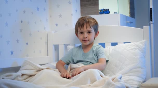Портрет милого мальчика, играющего с игрушками в постели перед сном. Дети играют с игрушками и веселятся — стоковое видео