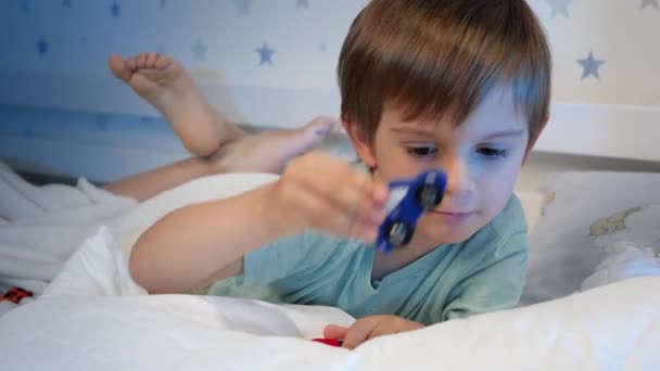 Portrait of little boy playing with two toy cars at bedtime. Toddler boy lying in bed and playing with cars — Stock Video