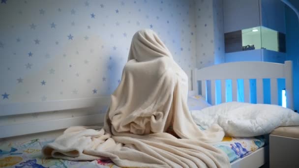 Медленное движение маленького мальчика, прячущегося под одеялом и выпрыгивающего. Дети играют и пугают людей по ночам — стоковое видео