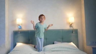 Mutlu, pijamalı bir çocuk gece yatmadan önce büyük bir yatakta zıplıyor. Geceleri uykusuz aktif çocuklar