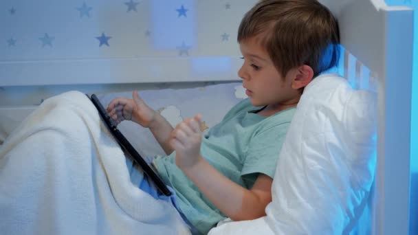 Szekrény a kisfiú táblagéppel néz rajzfilmeket, és játszik a táblagépen éjszaka, mielőtt aludni — Stock videók