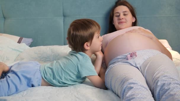 Junge schwangere Mutter mit dickem Bauch, die nachts mit ihrem älteren Sohn im Bett liegt. Familie hat gute Zeit zusammen und erwartet Baby — Stockvideo