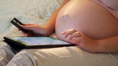 Elinde kocaman bir kredi kartı olan hamile bir kadının gece vakti tablet bilgisayarında e-mağazada online alışveriş yapması.