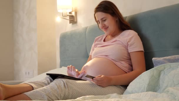Mosolygó terhes nő csinál online vásárlás tabletta számítógép, mielőtt aludni éjjel. — Stock videók