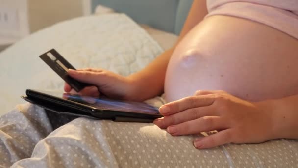 Primer plano de la mujer embarazada con el vientre grande que sostiene la tarjeta de crédito y el uso de la tableta para hacer compras en línea. Concepto de compras en línea y e-store en gadgets — Vídeo de stock